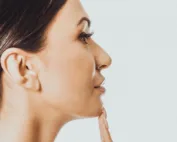 Perfil feminino com a mão no queixo (rinoplastia)