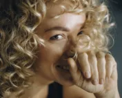 Mulher sorridente com a mão no rosto (rinoplastia no Porto e em Braga)